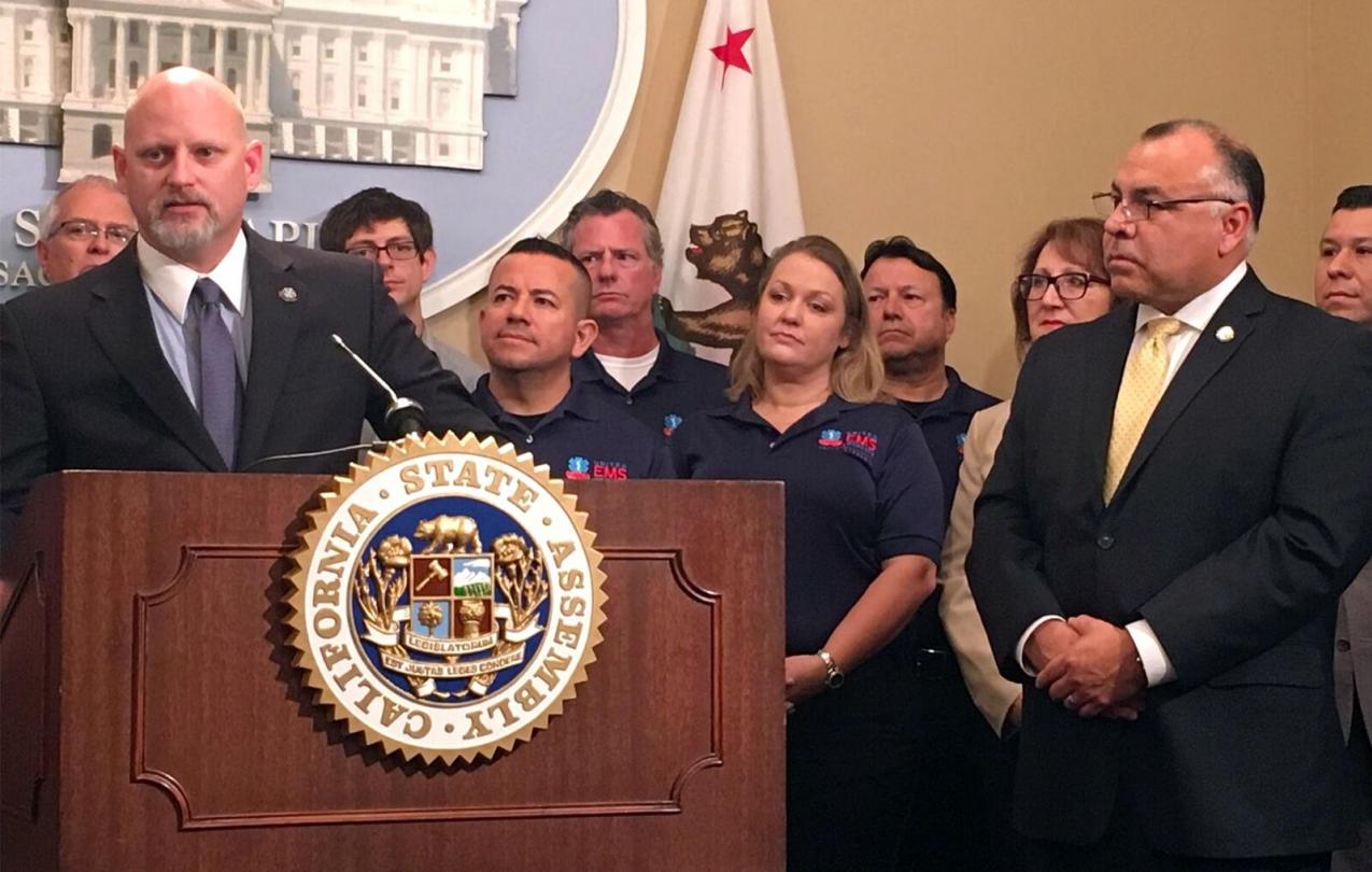 Jason Brollini, president of UEMSW/AFSCME Local 4911, speaks in support of AB263, the EMS Workers’ Bill of Rights, as the measure’s sponsor, Assemblymember Freddie Rodriguez (gold tie), looks on.