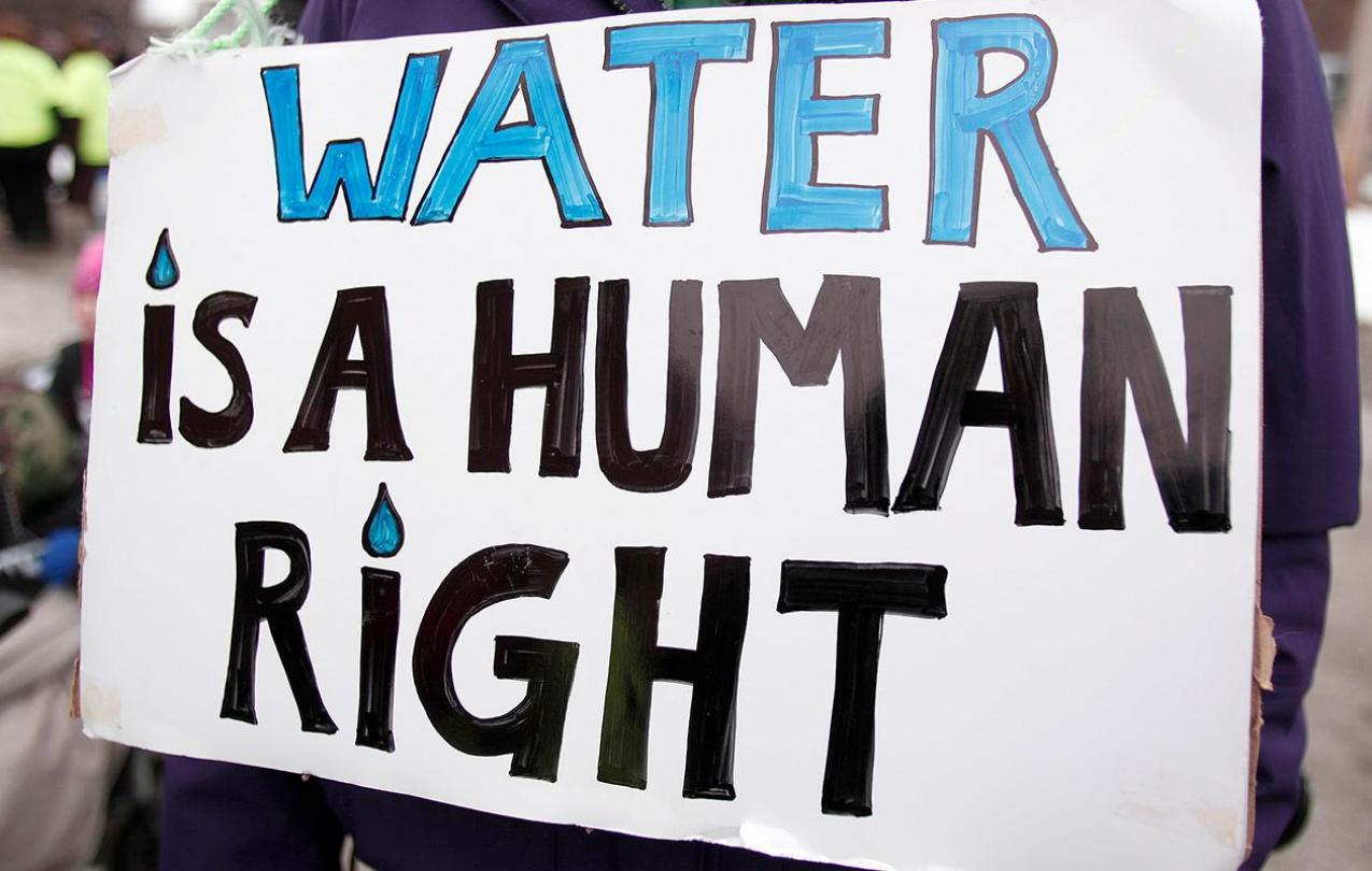 Image of a protest poster with "WATER IS A HUMAN RIGHT" written in bold letters.