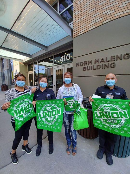 WFSE members & Maleng Cafe employees Ghenet Habtemnichael, Marianna Tereko, Aster Morrow, and Christian Cisneros each hold WFSE green items- three large bandanas and a folder outside the Norm Maleng Building. They are wearing masks.